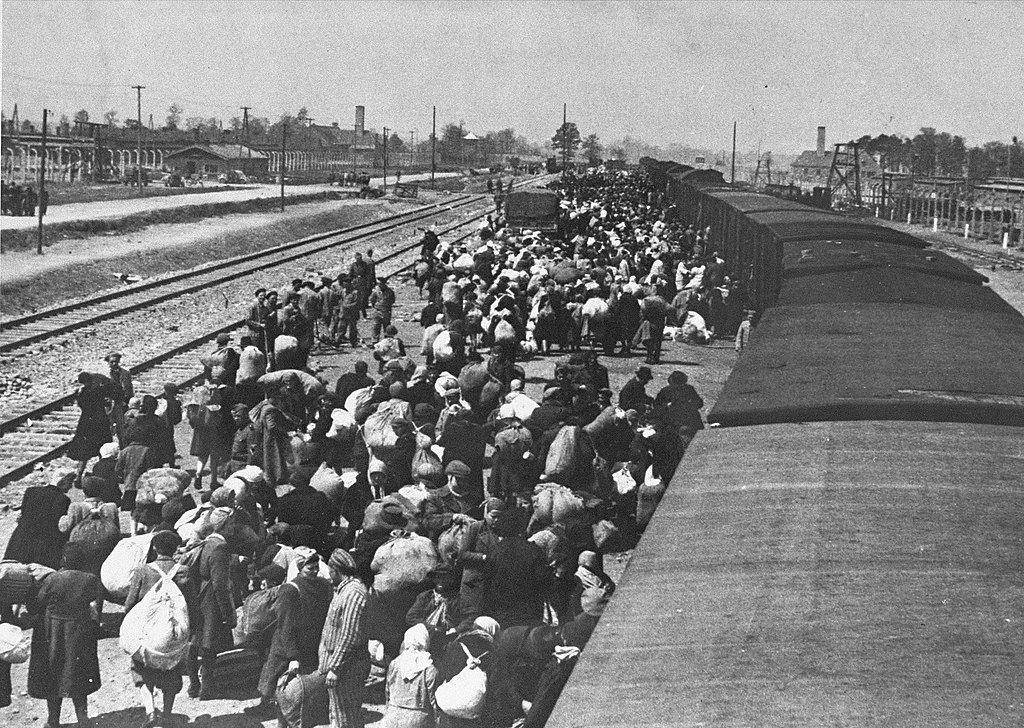 Rampe bondée d'Auschwitz-Birkenau en mai 1944. Les cheminées à l'horizon sont les crématoires situés à côté des chambres à gaz.