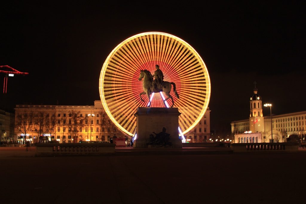 Monument à Lyon : La statue du Roi Soleil devant la grande roude illuminée de la place de Bellecour.