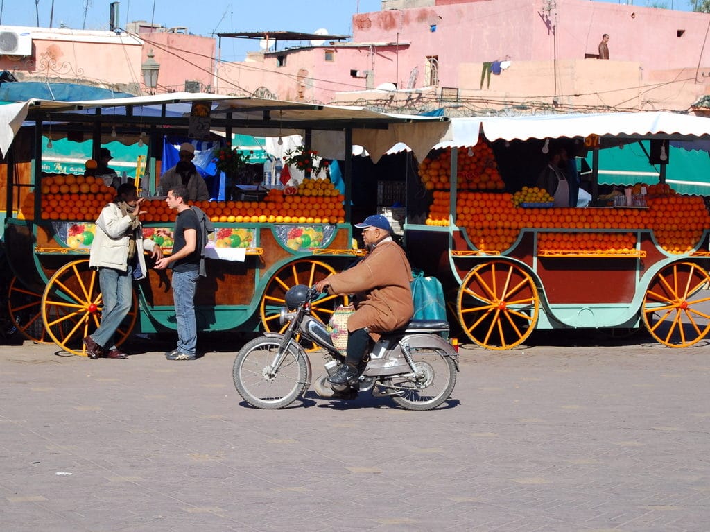 Pratique à Marrakech : Un homme en scooter devant les vendeurs de jus de fruits .